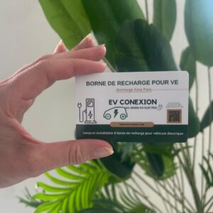 Hand holding a white EV charging card with 'EV CONEXION' and charging icon, plant leaves in the background.