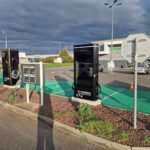 Electric vehicle charging station with two black units in a parking lot beside a green bike lane.